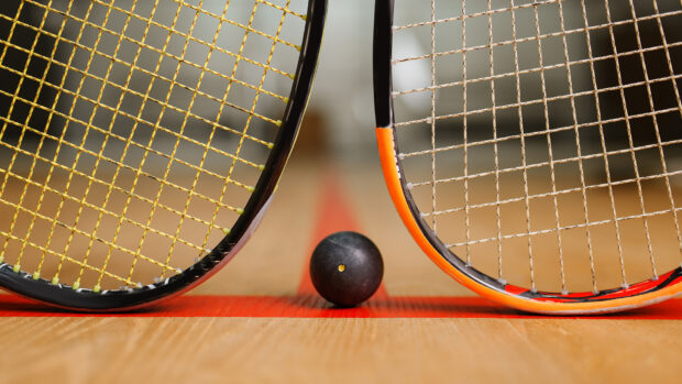 Two squash rackets and a black squash ball on a wooden court with a red line