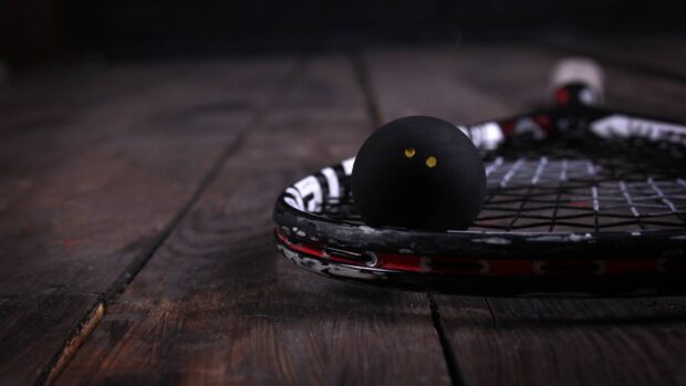A squash ball resting on a squash racket on a wooden floor in HD quality