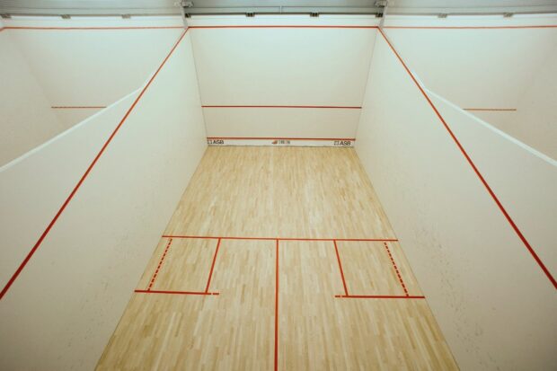 An empty squash court with wooden floor and marked lines for sport play