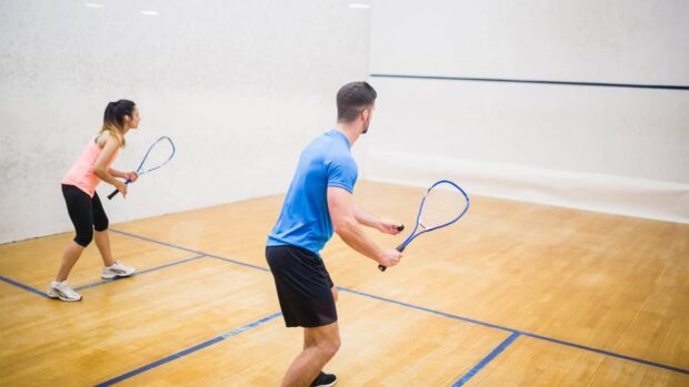 A man and a woman playing squash sport on an indoor court with rackets in action
