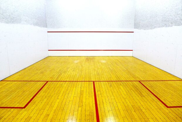 An empty squash court with wooden floor and red boundary lines