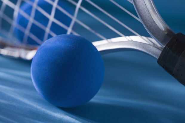Blue squash ball close to a squash racket on a blue court surface