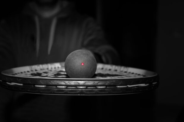 Squash ball resting on a racket captured in a dark setting
