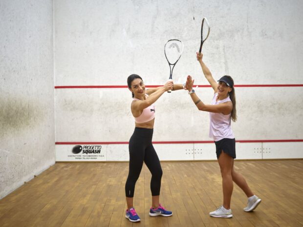 Two female athletes playing squash sport on the court with rackets smiling