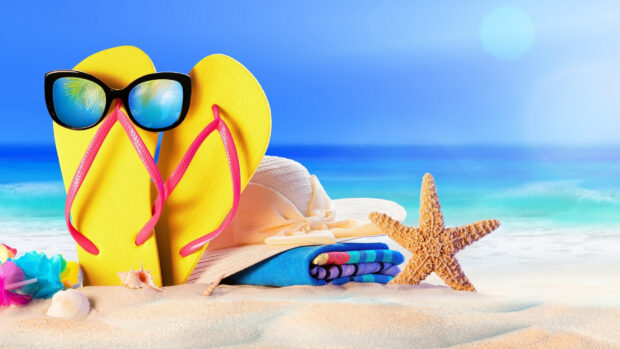 A starfish lying on sand near beach accessories including yellow flip flops and a sun hat