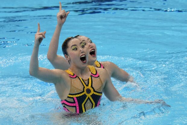 Two synchronized swimmers performing in a pool with colorful costumes