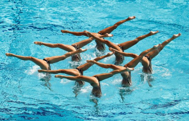 A synchronized swimming team performing a coordinated leg lift routine in a pool