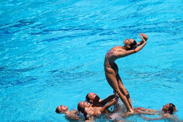 A synchronized swimming team performing a lift move in a clear blue pool