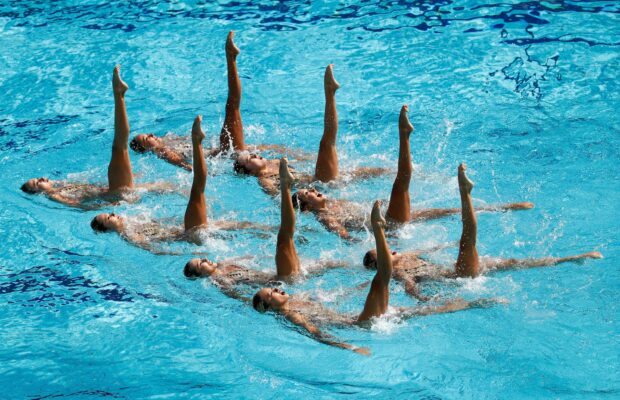 A synchronized swimming team performing a precise routine in a clear blue pool