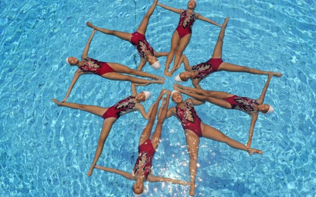 Six synchronized swimmers performing a routine holding hands in a pool