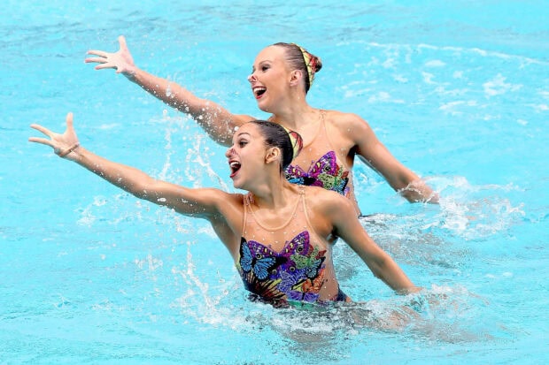 Two synchronized swimmers performing in colorful costumes displaying coordinated movements in the pool