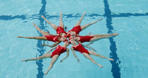A synchronized swimming team in red swimsuits performs a formation in a clear blue pool
