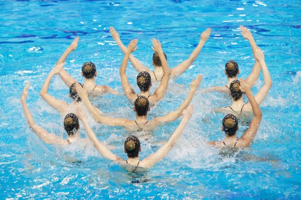 A synchronized team performing a swimming routine in a pool with water splashing around