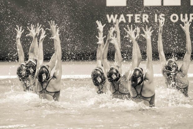 Synchronized swimming athletes performing a coordinated routine in water splash