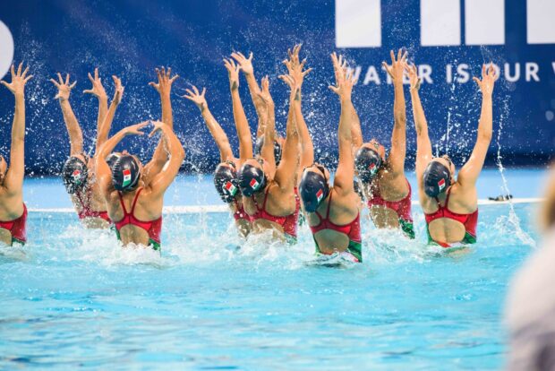 Synchronized swimming team performing a routine with raised arms in a pool