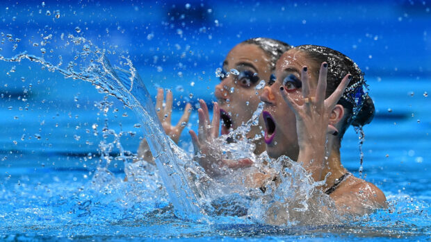Two synchronized swimmers performing a routine with expressive faces and water splashing around them