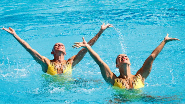 Two synchronized swimmers performing in the pool with joyful expressions