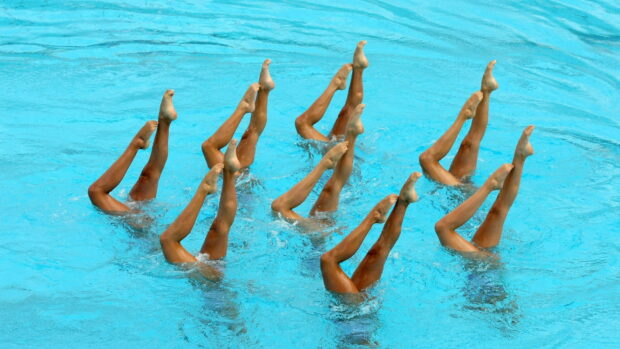 A group of synchronized swimmers performing a routine with their legs raised above the water