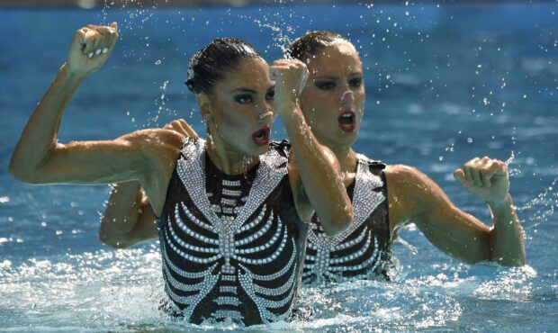 Two synchronized swimming athletes perform an intense routine in the pool with matching costumes