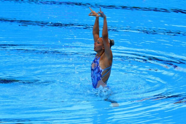 A synchronized swimmer performing a graceful routine in a clear blue pool