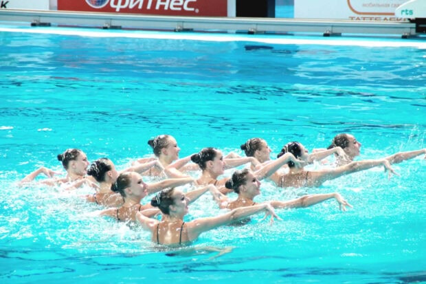 A synchronized swimming team performing a coordinated routine in a bright blue pool