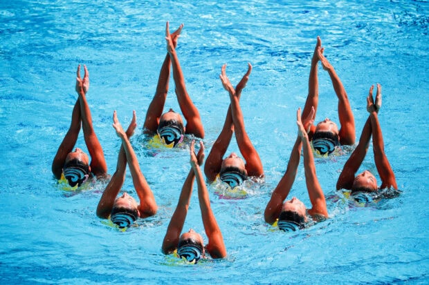 A synchronized swimming team performing a coordinated routine in the pool with hands raised above water