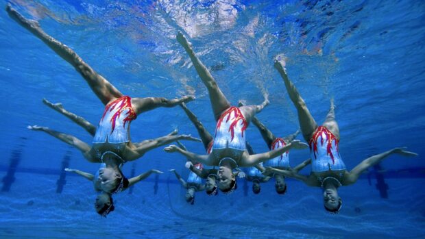 A synchronized swimming team performing a routine underwater in a pool in matching swimsuits