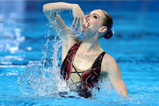 A synchronized swimmer performing an artistic move with water splashing around her in a pool