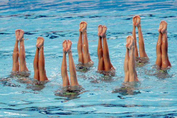 A synchronized swimming team performing a routine with legs extended out of the water in unison