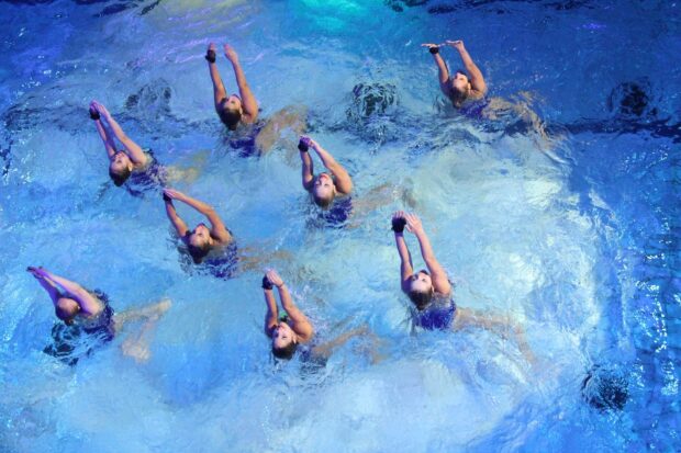 A synchronized team performing a routine in a blue swimming pool