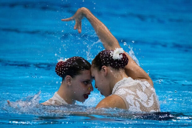 Two synchronized swimmers performing a coordinated routine in the pool with artistic hand movements