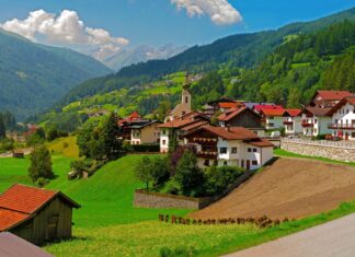 A peaceful town surrounded by green hills and mountains under a bright blue sky