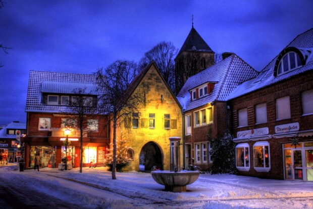 Snowy town street at dusk with historic buildings and warm lights
