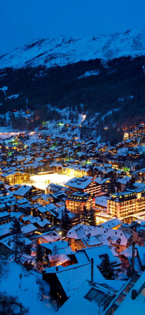 Snow covered town nestled in the mountains with glowing lights during blue hour