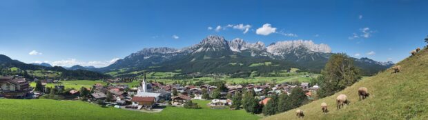 A peaceful town surrounded by green fields and towering mountains under a clear blue sky
