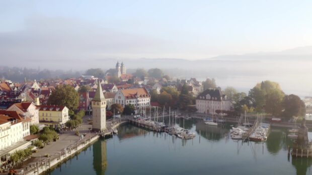 A scenic town harbor with boats and historic buildings under morning mist