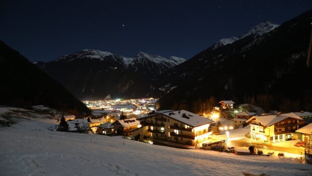 A snowy town nestled in a mountain valley with bright lights illuminating the night sky