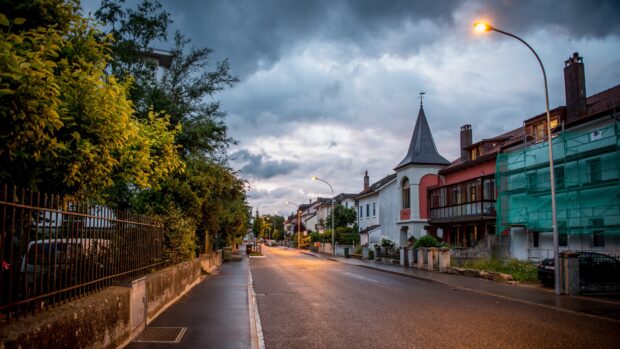 Quiet town street with houses and trees under cloudy sky at dusk