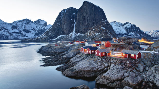 Small town nestled among rocky shores with snow capped mountains in the background