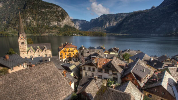 A peaceful town with traditional houses and a tall steeple by a serene lake surrounded by mountains