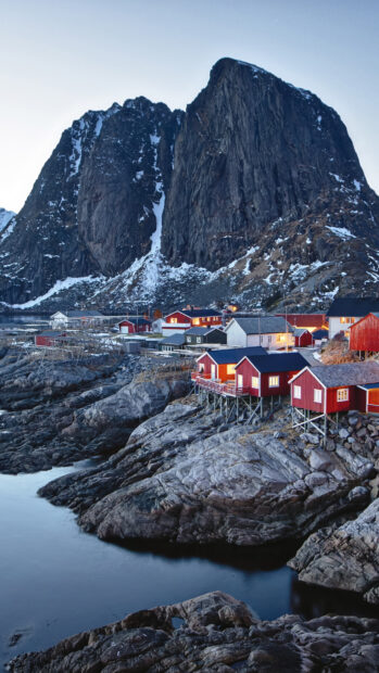 Small town nestled on rocky shore with large mountain in the background