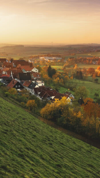 A peaceful town surrounded by autumn trees and rolling green hills at sunset