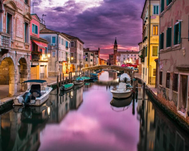 Venice canal at sunset with historic buildings and boats reflecting on the water