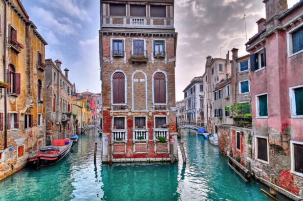 Historic Venice building between two canals with boats and clear water