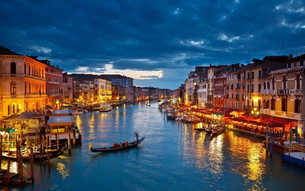 Evening gondola ride through Venice canal with illuminated buildings and cloudy sky