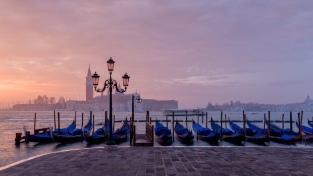 Early morning gondola boats lined up by the Venice waterfront under a pastel sky