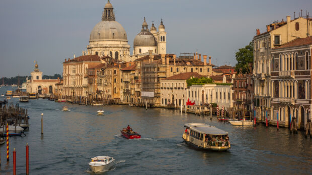Historic Venice cityscape with boats traveling on the canal and domed architecture in warm light