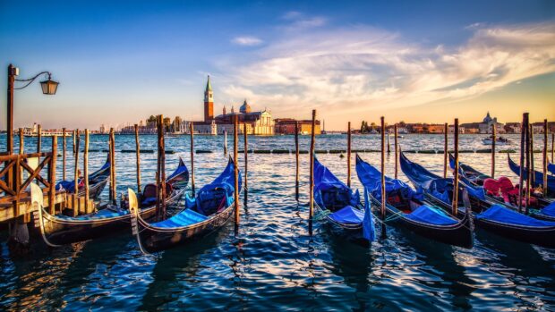 Venice gondolas moored by the wooden dock with Venice skyline in the background at sunset