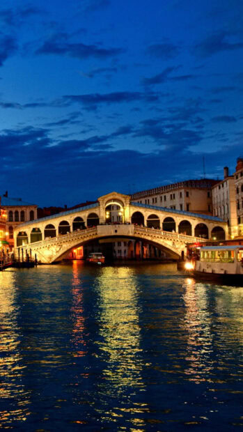 Venetian canal with illuminated bridge at dusk reflecting on water