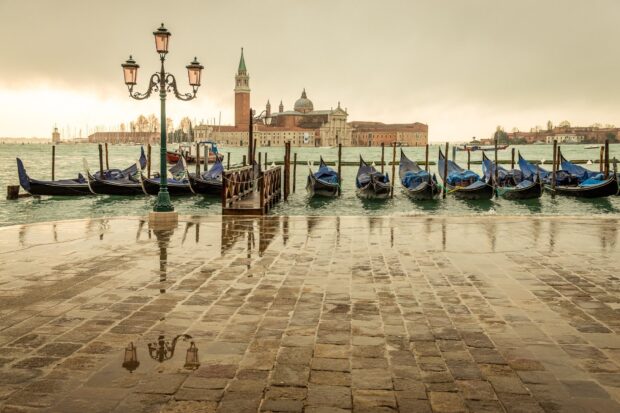 Gondolas docked by a rainy waterfront in Venice with historic buildings in the background
